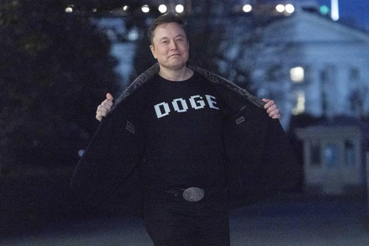 Elon Musk flashes his T-shirt that reads “DOGE” to the news media as he walks on South Lawn of the White House, in Washington, Sunday, March 9, 2025.