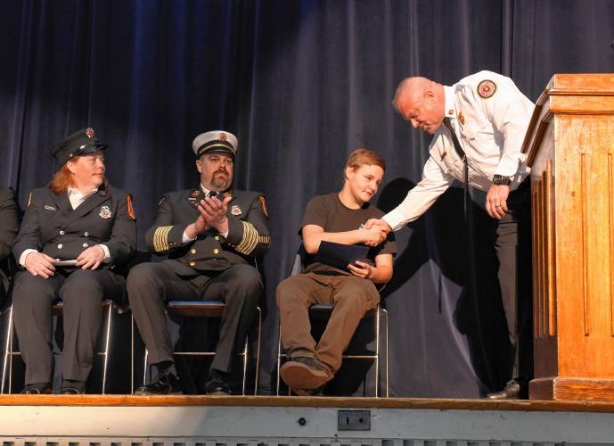 Ralph C. Mahar Regional School student Joel Wilkey is honored for his quick thinking during a chimney fire by State Fire Marshal Jon Davine during an assembly at the school Friday morning. At left is Orange firefighter Meaghan Ahearn and Orange Fire Chief James Young.