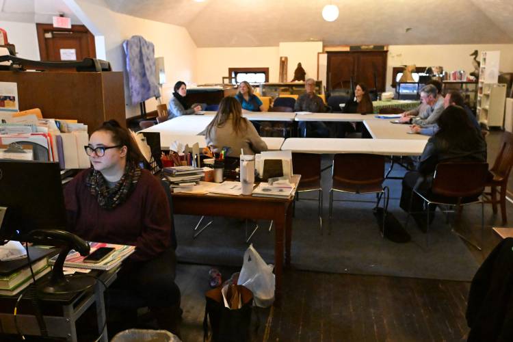 Ellen Williams, left, children’s programming assistant at the Carnegie Public Library in Turners Falls, works on the second floor of the library while a meeting about a new library takes place behind her.